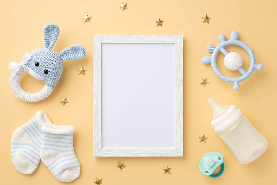 A blank photo frame placed in the center with baby accessories surrounding it in a pastel-colored background.